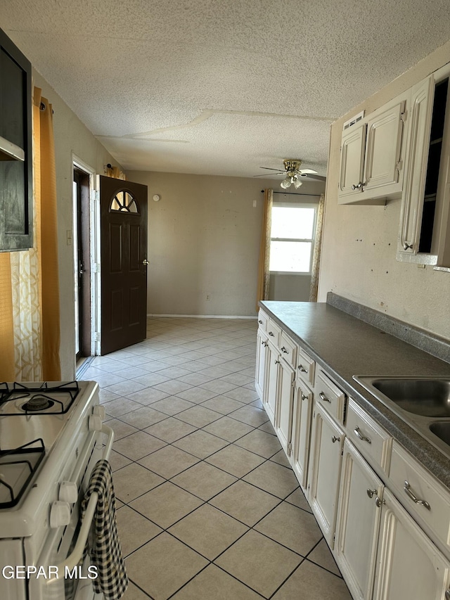 7800 Monterrey Dr, El Paso, TX 79915 - kitchen featuring white gas range oven, dark countertops, a textured ceiling, ceiling fan, and light tile patterned floors