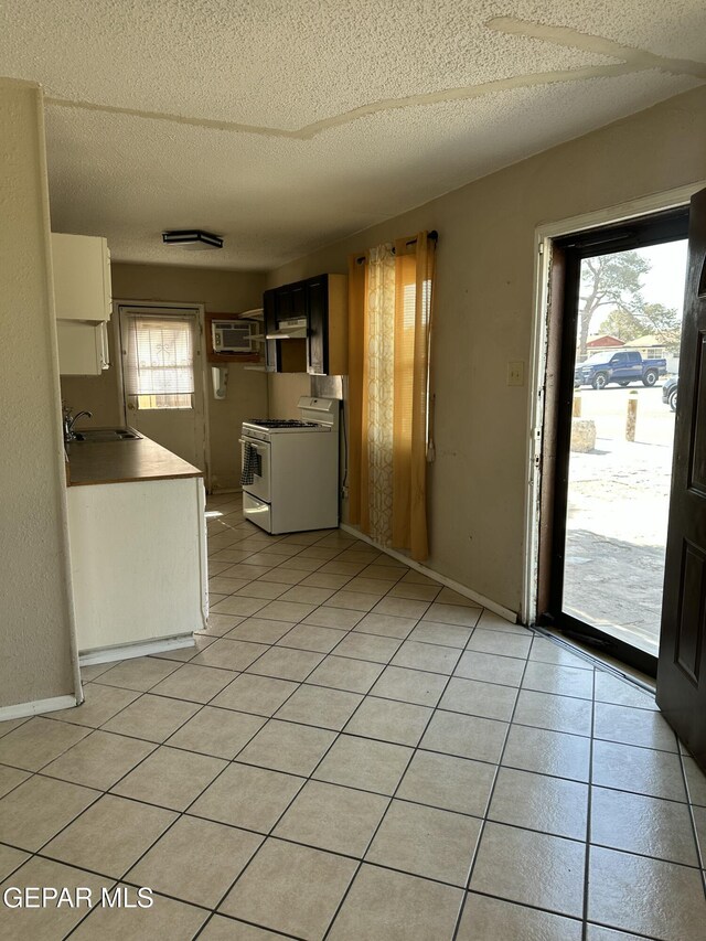 7800 Monterrey Dr, El Paso, TX 79915 - kitchen featuring white gas stove, a textured ceiling, a sink, a wall mounted air conditioner, and light tile patterned floors