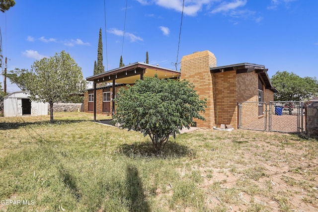 9913 Bomarc St, El Paso, TX 79924 - rear view of house with brick siding, a gate, a chimney, and a lawn