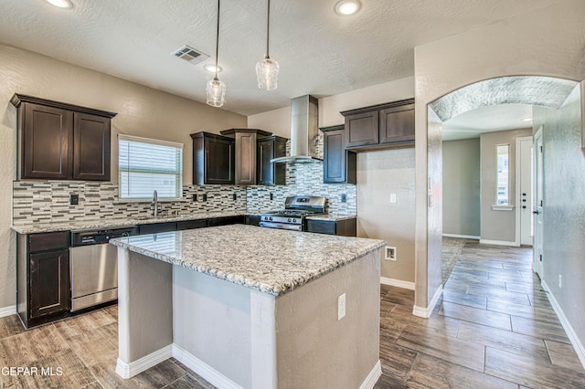 12772 Silver Streak Ave, El Paso, TX 79928 - kitchen with stainless steel appliances, wall chimney range hood, dark brown cabinetry, arched walkways, and a textured ceiling