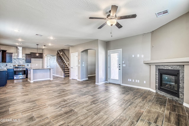 12772 Silver Streak Ave, El Paso, TX 79928 - unfurnished living room with arched walkways, ceiling fan, stairs, a stone fireplace, and wood finished floors
