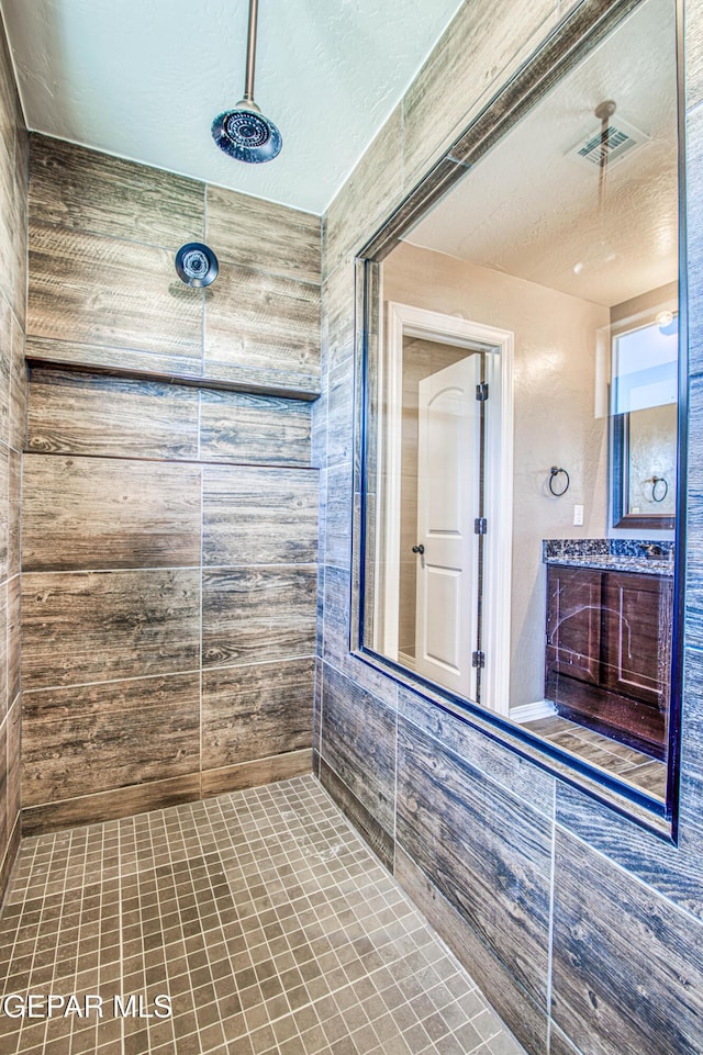 12772 Silver Streak Ave, El Paso, TX 79928 - bathroom featuring tiled shower, vanity, wood walls, and a textured ceiling