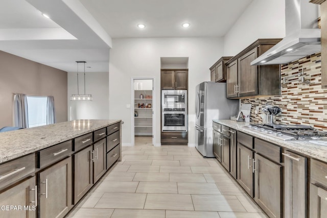 2367 Enchanted Peaks Ln, El Paso, TX 79911 - kitchen with stainless steel appliances, wall chimney range hood, backsplash, light stone counters, and dark brown cabinetry