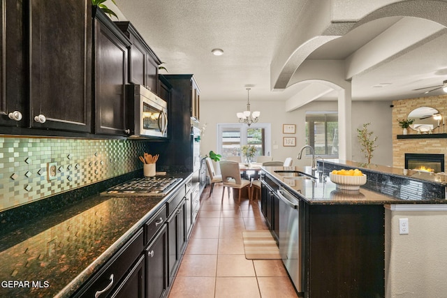 14382 Karen Point Ct, El Paso, TX 79938 - kitchen with a sink, stainless steel appliances, dark stone countertops, a fireplace, and light tile patterned flooring