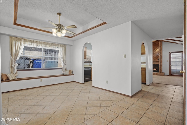 4513 Gen Maloney Cir, El Paso, TX 79924 - unfurnished room featuring a textured ceiling, arched walkways, ceiling fan, a brick fireplace, and a tray ceiling