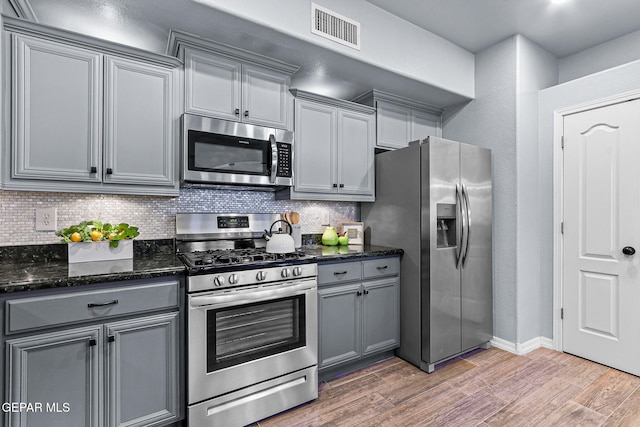14045 Tower Point Way, El Paso, TX 79938 - kitchen with stainless steel appliances, gray cabinetry, light wood-type flooring, tasteful backsplash, and dark stone counters