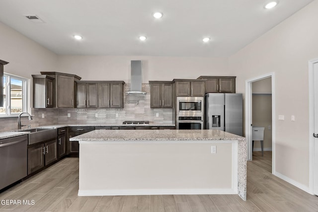 3952 Aspiration St, El Paso, TX 79938 - kitchen featuring wall chimney exhaust hood, appliances with stainless steel finishes, a kitchen island, dark brown cabinets, and light wood-type flooring