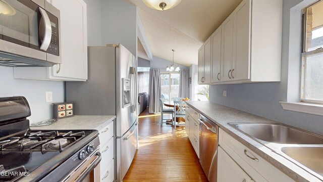 684 Abington Dr, El Paso, TX 79912 - kitchen with appliances with stainless steel finishes, a chandelier, lofted ceiling, a sink, and light wood-style flooring