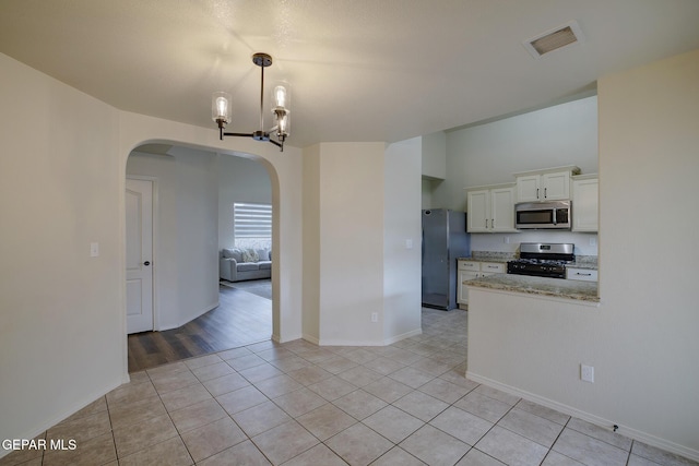 7044 Eagle Nest Ct, El Paso, TX 79934 - kitchen with stainless steel microwave, range with gas cooktop, freestanding refrigerator, arched walkways, and white cabinets