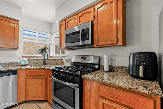 1328 Morgan Marie St, El Paso, TX 79936 - kitchen with appliances with stainless steel finishes, a sink, light tile patterned floors, brown cabinets, and dark stone counters