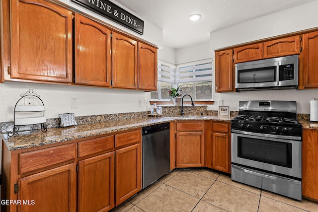 1328 Morgan Marie St, El Paso, TX 79936 - kitchen with stainless steel appliances, a sink, dark stone countertops, light tile patterned flooring, and brown cabinetry