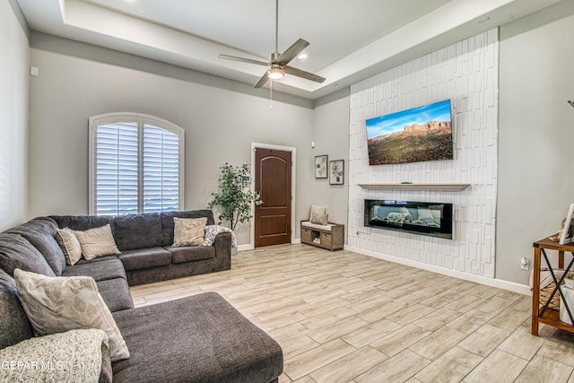 12826 Osmotherly Ave, El Paso, TX 79928 - living area featuring a tray ceiling, a ceiling fan, light wood-type flooring, a large fireplace, and baseboards