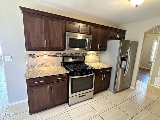 7217 Long Meadow Dr, El Paso, TX 79934 - kitchen featuring stainless steel appliances, arched walkways, backsplash, dark brown cabinets, and a textured ceiling