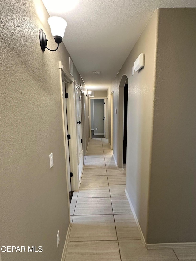 7217 Long Meadow Dr, El Paso, TX 79934 - hall featuring arched walkways, light tile patterned flooring, a textured wall, and baseboards