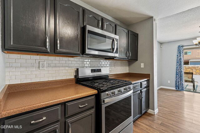 11912 Mesquite Miel Dr, El Paso, TX 79938 - kitchen featuring stainless steel appliances, light wood finished floors, a textured ceiling, dark countertops, and decorative backsplash