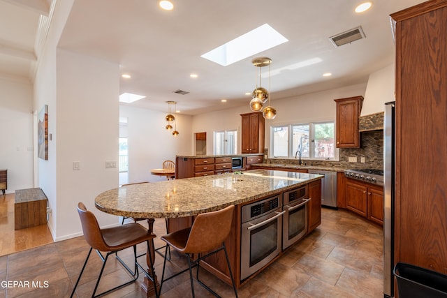 1013 Singing Hills Dr, El Paso, TX 79912 - kitchen featuring a skylight, stainless steel appliances, brown cabinetry, a breakfast bar area, and a center island