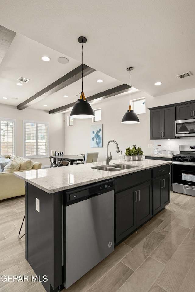 14924 Hill Ridge Ct, El Paso, TX 79938 - kitchen featuring appliances with stainless steel finishes, a kitchen island with sink, open floor plan, dark cabinets, and hanging light fixtures