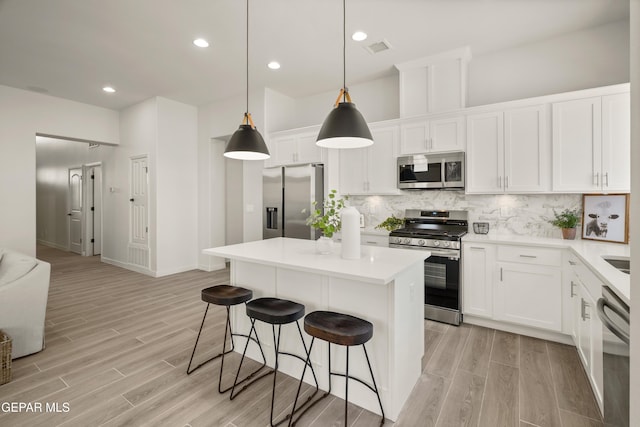 14932 Hill Ridge Ct, El Paso, TX 79938 - kitchen with appliances with stainless steel finishes, light wood-type flooring, a kitchen bar, decorative backsplash, and a kitchen island