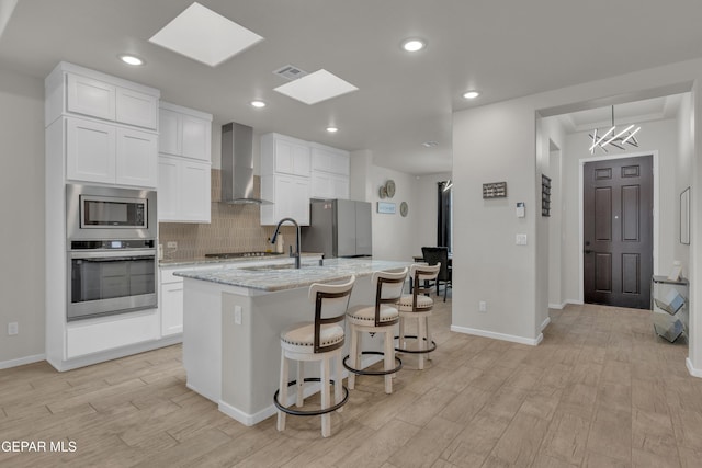 281 Farnborough St, Horizon City, TX 79928 - kitchen featuring stainless steel appliances, wall chimney range hood, light wood finished floors, a center island with sink, and a sink