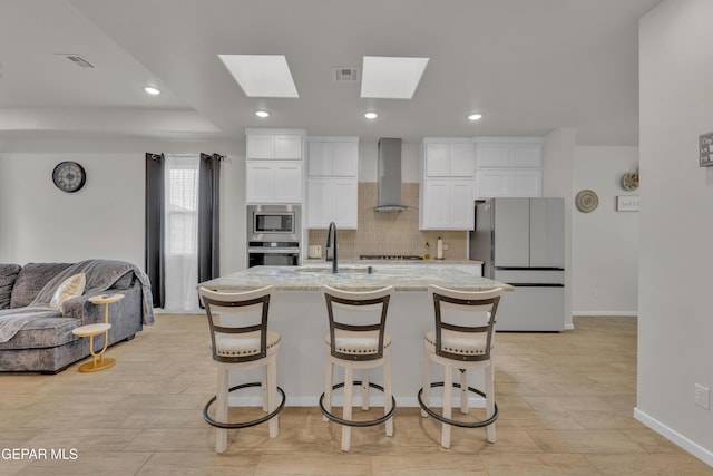 281 Farnborough St, Horizon City, TX 79928 - kitchen with stainless steel appliances, wall chimney range hood, white cabinets, decorative backsplash, and a breakfast bar