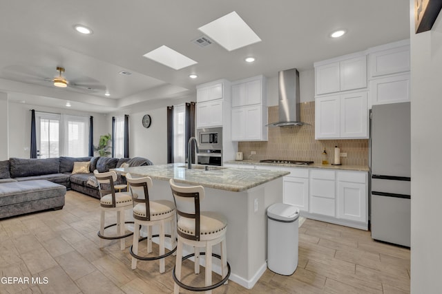 281 Farnborough St, Horizon City, TX 79928 - kitchen featuring stainless steel appliances, wall chimney exhaust hood, open floor plan, light wood-style floors, and white cabinets