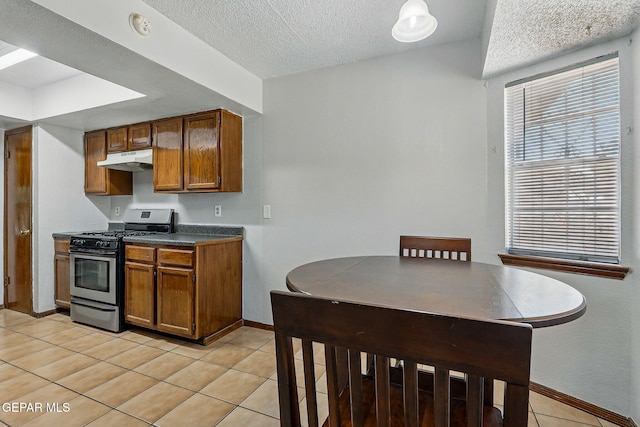 7721 Maya Ave, El Paso, TX 79912 - kitchen with gas stove, under cabinet range hood, brown cabinetry, baseboards, and light tile patterned floors