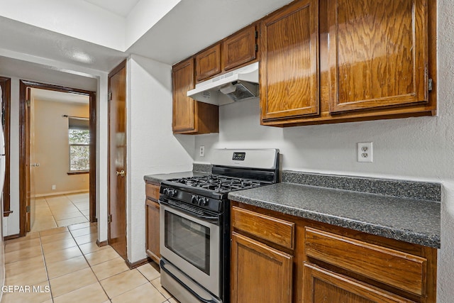 7721 Maya Ave, El Paso, TX 79912 - kitchen featuring under cabinet range hood, stainless steel range with gas cooktop, light tile patterned floors, dark countertops, and brown cabinetry