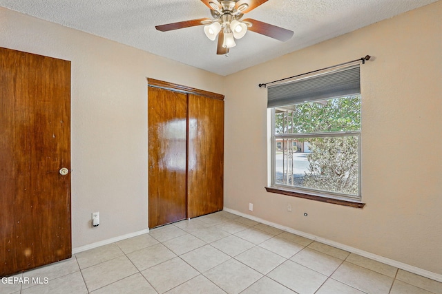 7721 Maya Ave, El Paso, TX 79912 - unfurnished bedroom with a textured ceiling, a closet, light tile patterned flooring, baseboards, and a ceiling fan