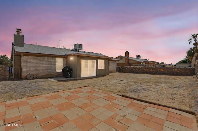 7721 Maya Ave, El Paso, TX 79912 - back of house at dusk featuring a patio area, a chimney, a fenced backyard, brick siding, and cooling unit