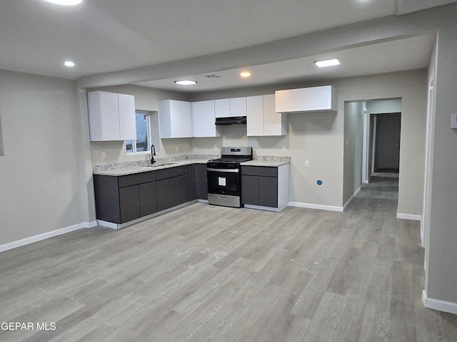 2917 Mobile Ave, El Paso, TX 79930 - kitchen with stainless steel gas range, under cabinet range hood, light countertops, white cabinetry, and light wood-type flooring