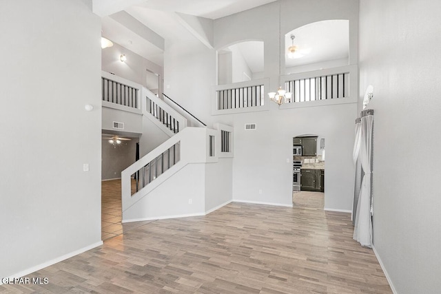 5429 Santiago Roque Dr, El Paso, TX 79934 - unfurnished living room with stairway, wood finished floors, arched walkways, a high ceiling, and a chandelier