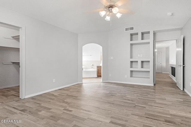 5429 Santiago Roque Dr, El Paso, TX 79934 - unfurnished living room featuring arched walkways, a ceiling fan, light wood-type flooring, built in features, and lofted ceiling