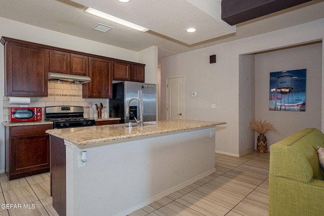 1916 William Caples St, El Paso, TX 79938 - kitchen featuring appliances with stainless steel finishes, under cabinet range hood, decorative backsplash, light stone counters, and a center island with sink