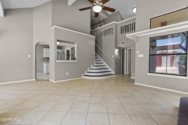 11765 Queens Garden Cir, El Paso, TX 79936 - unfurnished living room featuring high vaulted ceiling, a ceiling fan, tile patterned floors, arched walkways, and stairway