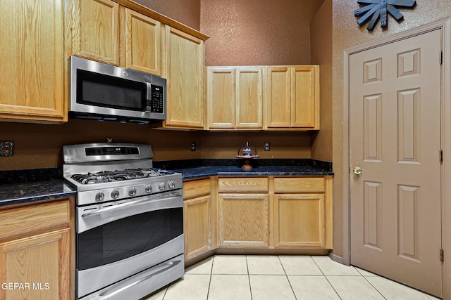 658 John Martin Ct, El Paso, TX 79932 - kitchen with stainless steel appliances, light brown cabinetry, a textured wall, light tile patterned floors, and dark stone countertops