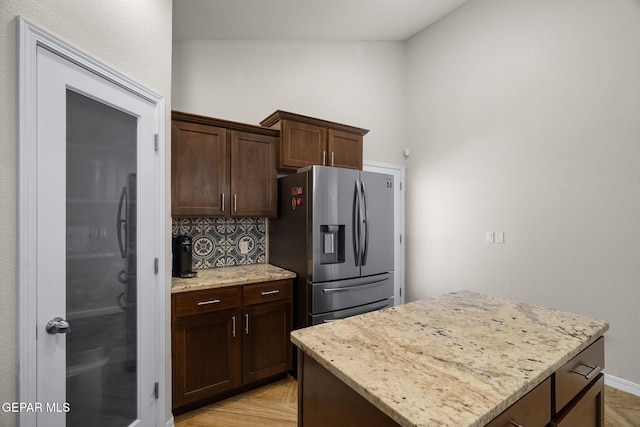 14183 Peyton Edwards Ave, El Paso, TX 79938 - kitchen featuring stainless steel refrigerator with ice dispenser, light stone countertops, decorative backsplash, dark brown cabinets, and a center island