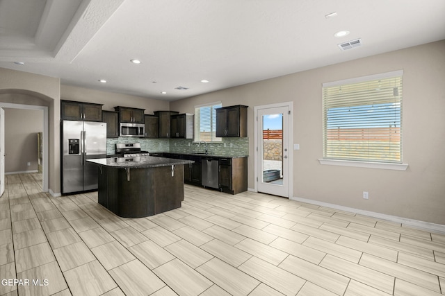 12632 Katherine Brennand Rd, El Paso, TX 79928 - kitchen featuring appliances with stainless steel finishes, a center island, backsplash, arched walkways, and dark brown cabinetry