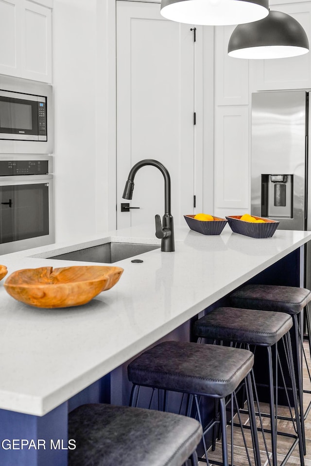 1449 Indigo Sky St, El Paso, TX 79928 - kitchen featuring stainless steel appliances, a sink, a breakfast bar, white cabinetry, and light countertops