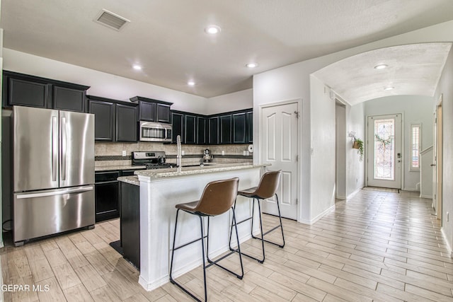 7517 Red Cedar Dr, El Paso, TX 79911 - kitchen featuring stainless steel appliances, dark cabinetry, arched walkways, light wood-type flooring, and backsplash