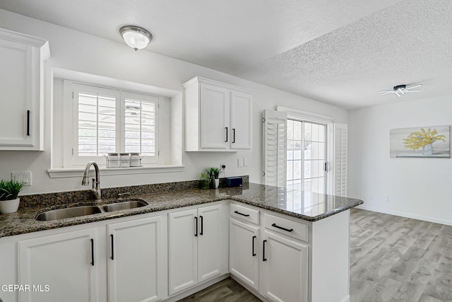 6929 Canyon View Ln, El Paso, TX 79912 - kitchen featuring a sink, a peninsula, white cabinets, light wood finished floors, and dark stone countertops