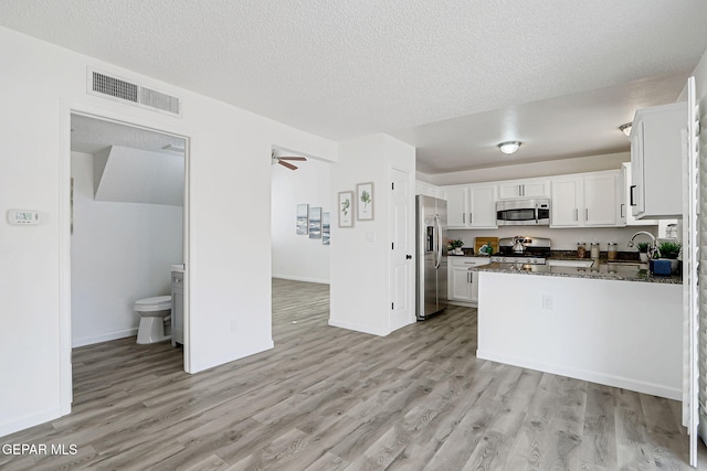6929 Canyon View Ln, El Paso, TX 79912 - kitchen with appliances with stainless steel finishes, light wood-type flooring, white cabinetry, a textured ceiling, and dark stone countertops