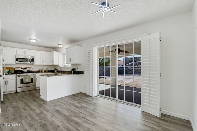 6929 Canyon View Ln, El Paso, TX 79912 - kitchen featuring appliances with stainless steel finishes, light wood finished floors, dark countertops, white cabinetry, and a textured ceiling