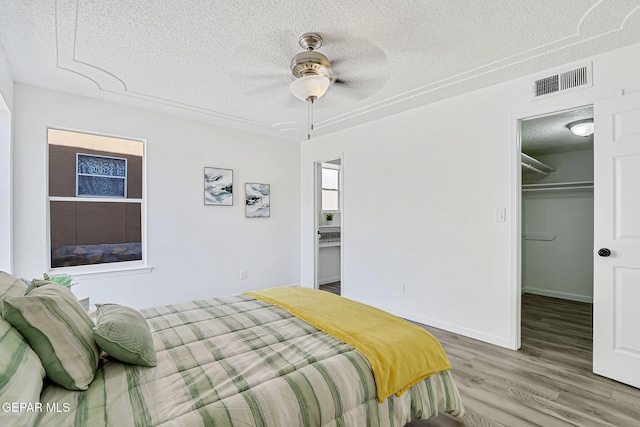 6929 Canyon View Ln, El Paso, TX 79912 - bedroom with a textured ceiling, light wood-type flooring, a walk in closet, a closet, and ceiling fan