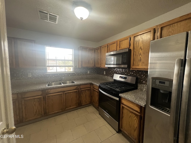 10256 Valle Suave Dr, El Paso, TX 79927 - kitchen featuring appliances with stainless steel finishes, a sink, brown cabinetry, tasteful backsplash, and light tile patterned flooring