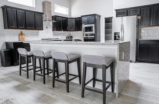 3920 Aspiration St, El Paso, TX 79938 - kitchen featuring stainless steel appliances, wall chimney range hood, dark cabinetry, and tasteful backsplash