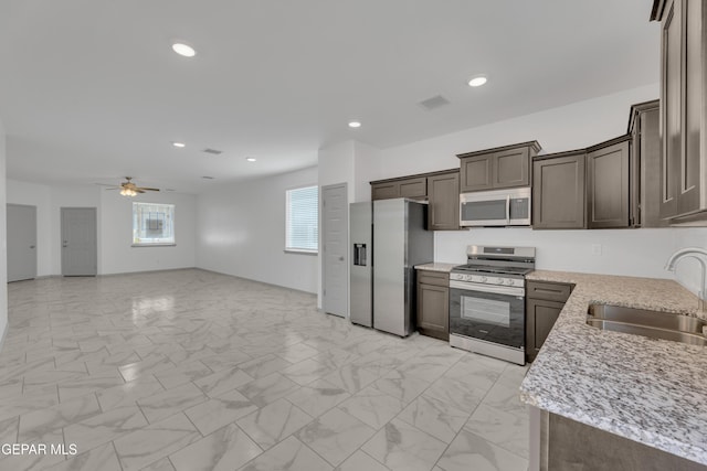 15221 Apex Ct, El Paso, TX 79938 - kitchen with appliances with stainless steel finishes, a ceiling fan, dark brown cabinetry, light marble finish floors, and light stone counters