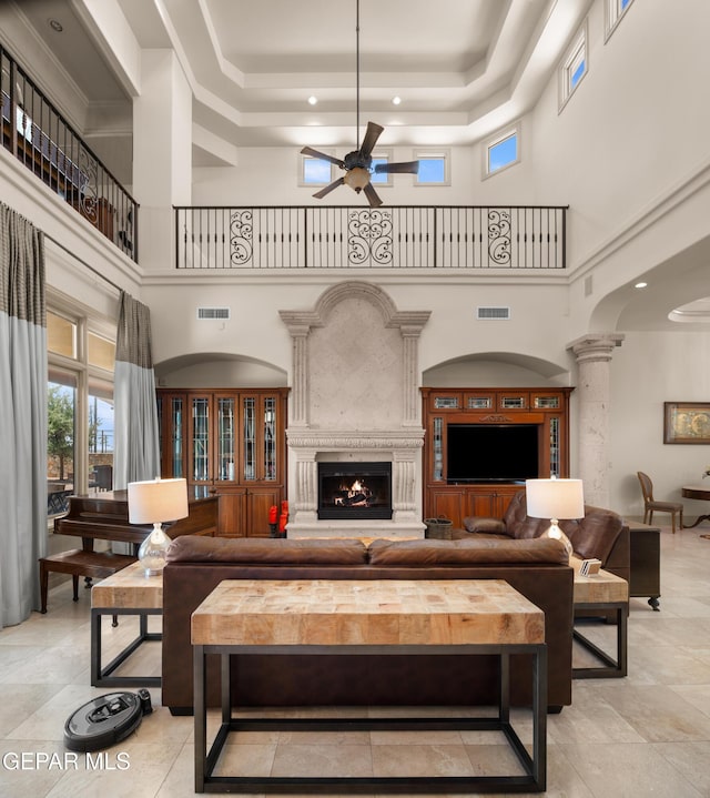 6572 Tuscany Ridge Dr, El Paso, TX 79912 - living room featuring ceiling fan, a raised ceiling, a towering ceiling, ornate columns, and a warm lit fireplace