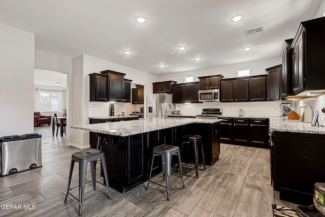 12749 Iron Falls Dr, Horizon City, TX 79928 - kitchen with appliances with stainless steel finishes, wood finish floors, backsplash, a kitchen bar, and recessed lighting