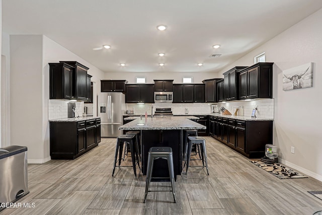 12749 Iron Falls Dr, Horizon City, TX 79928 - kitchen featuring appliances with stainless steel finishes, a breakfast bar area, backsplash, light stone countertops, and recessed lighting