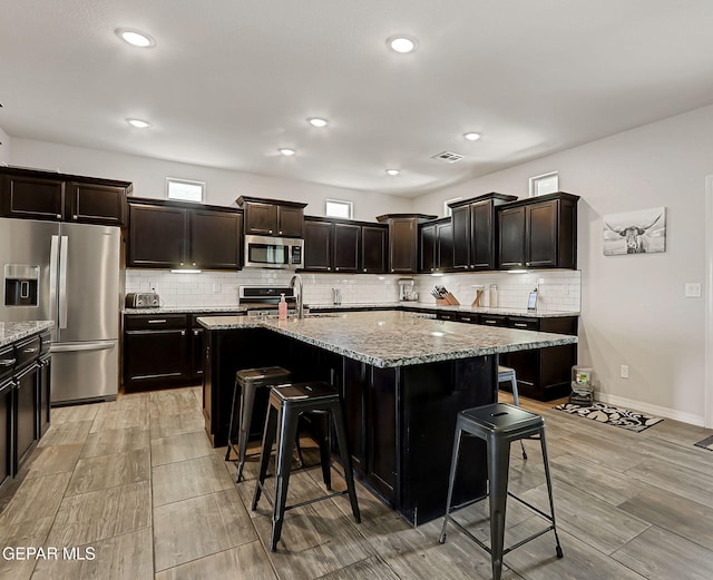 12749 Iron Falls Dr, Horizon City, TX 79928 - kitchen with appliances with stainless steel finishes, a breakfast bar area, backsplash, light stone countertops, and a sink